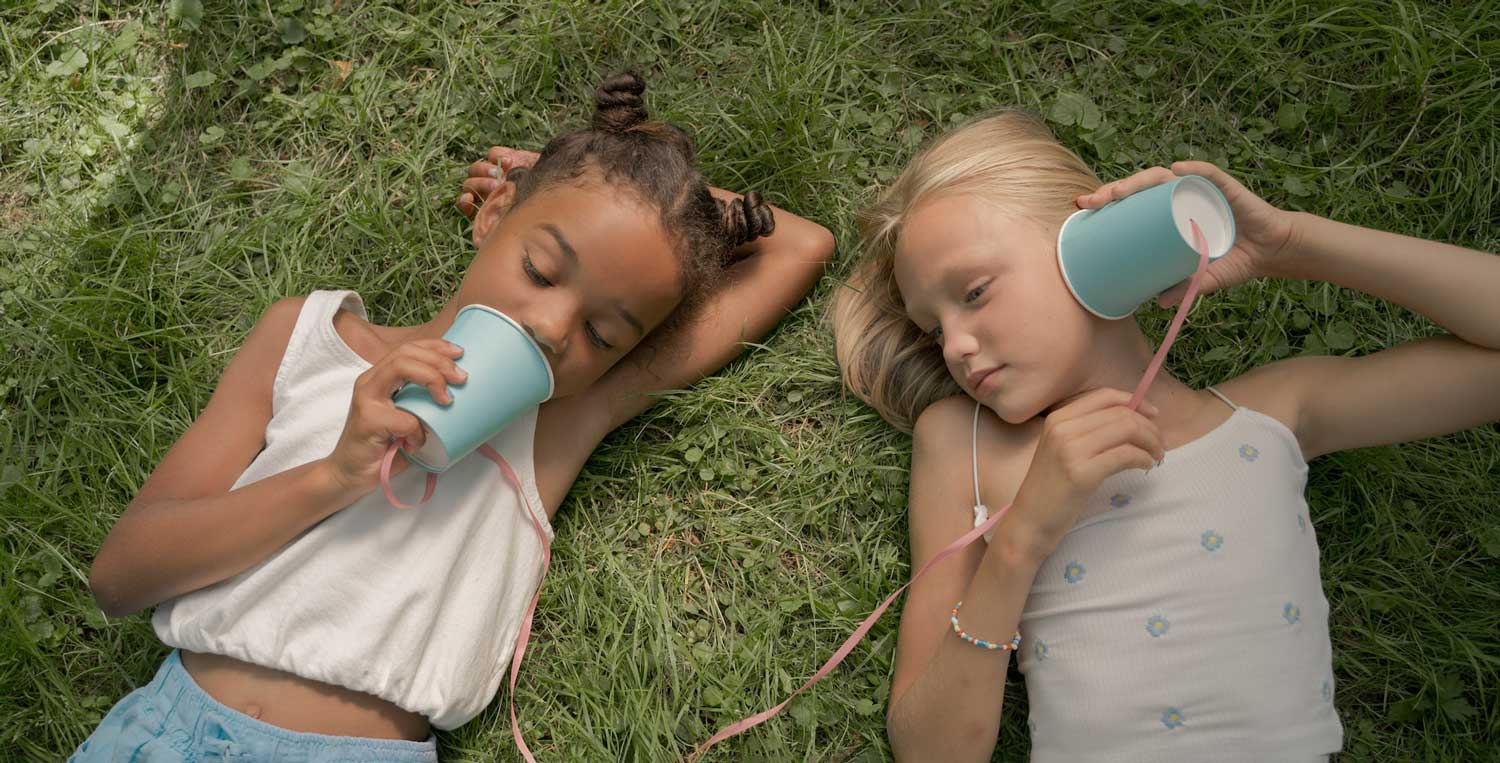 two girls lying in the grass playing tin can telephone